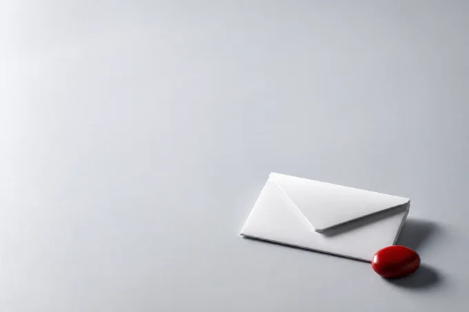 A simple blank envelope and red ceramic pebble on a quiet gray surface
